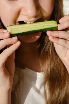Kid bites cucumber, close-up, unrecognizable face. Stock Photos