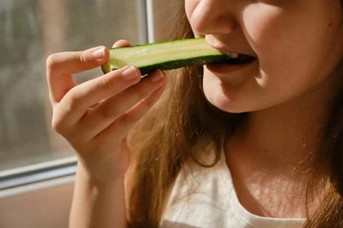 Kid bites cucumber, close-up, unrecognizable face. Stock Photos