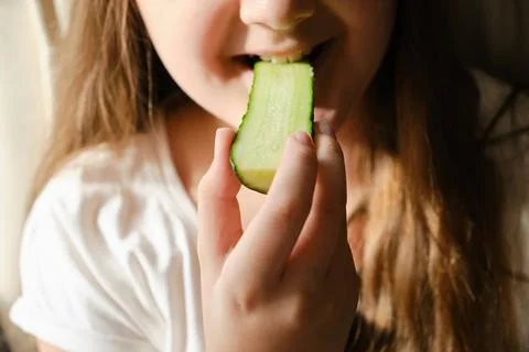 Kid bites cucumber, close-up, unrecognizable face. Stock Photos