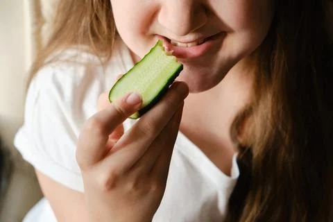 Kid bites cucumber, close-up, unrecognizable face. Stock Photos