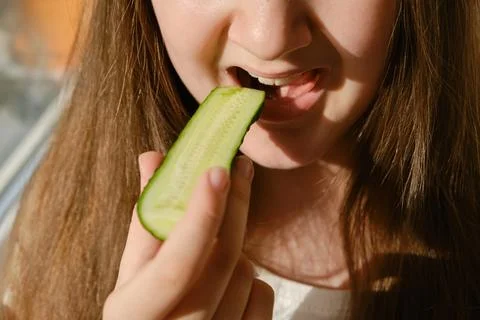 Kid bites cucumber, close-up, unrecognizable face. Stock Photos