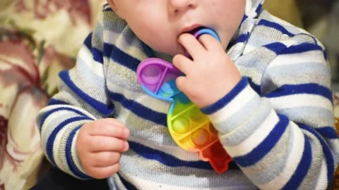 Kid boy of 1.5 years gnaws pop it toy. Eruption of deciduous teeth in child Stock Footage 166445821