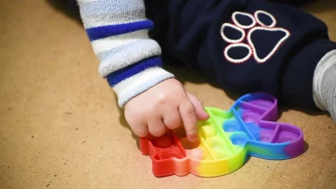 Kid boy of 1.5 years plays with pop it toy. Boy presses on colorful squishy soft 動画素材 166445685