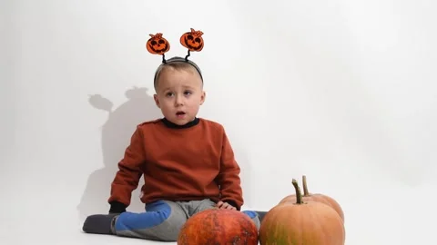 Kid boy of 3 years  sits at halloween pumpkins and catches balloon. Halloween Stock Footage 253990713