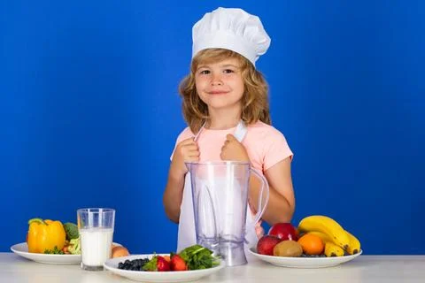Kid boy in chef hat and apron cooking preparing meal. Little cook with Stock Photos