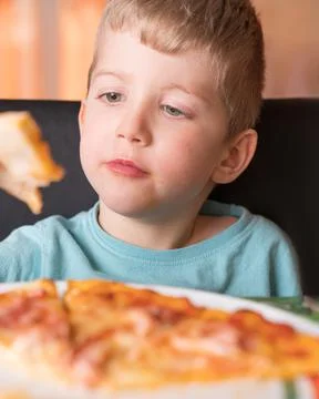 Kid boy eats pizza sitting at the table 写真素材