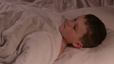 Kid boy with eyes open cannot sleep at night in a bed in the bedroom and dreams Stock Footage 263865716