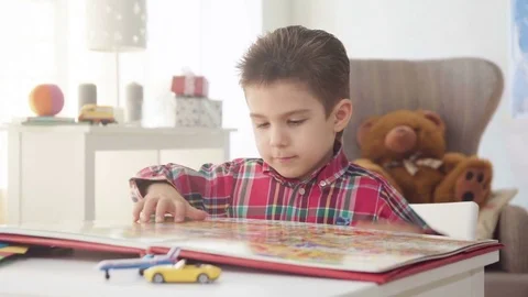 Kid boy look and examine book with color pictures with interest and fantasy Stock Footage 78201014