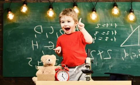 Kid boy near microscope in classroom, chalkboard on background. First former Stock Photos
