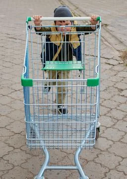 Kid boy pushing empty shopping cart at parking lot Stock Photos