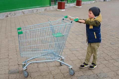 Kid boy pushing empty shopping cart at parking lot Stock Photos