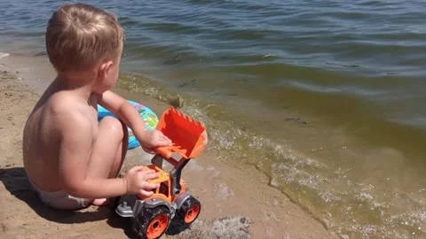 Kid boy  at the river coast plays with sand and toy. Summer leisure time. Family Stock Footage 249694222