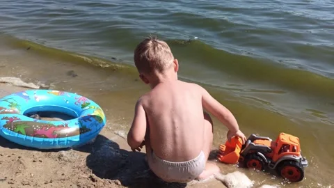 Kid boy  at the river coast plays with sand and toy. Summer leisure time. Family Stock Footage 249694407