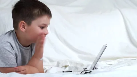 Kid boy using digital tablet technology device lying on bed alone. Child doin Stock Footage 136102471