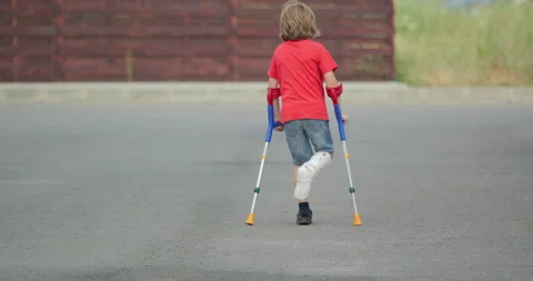 Kid with broken leg in plaster cast, walking with medical orthopedic crutches Stock Footage 298851494