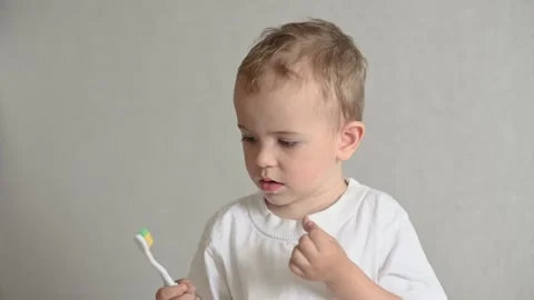 The kid is brushing his teeth with a toothbrush on a gray background. Oral Stock-Footage 244923423