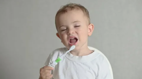 The kid is brushing his teeth with a toothbrush on a gray background. Oral Stock Footage 244923457