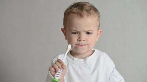 The kid is brushing his teeth with a toothbrush on a gray background. Oral Stock-Footage 246489037