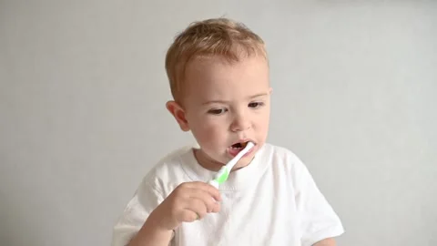 The kid is brushing his teeth with a toothbrush on a gray background. Oral Stock-Footage 246489051