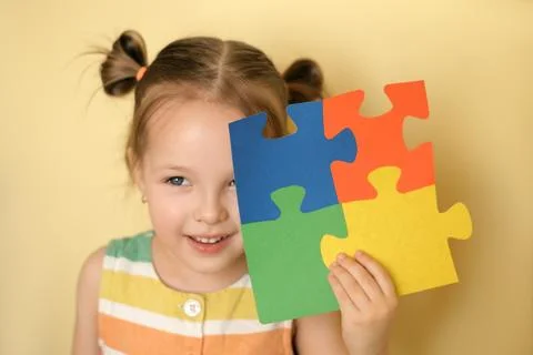 Kid cheerfully while closing eye holding puzzle of colorful details in hand Stock Photos
