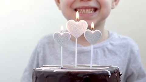 Kid child blowing candles light flame from silver glitter heart shape Stock Footage 222000740