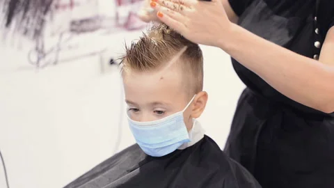 Kid client in protective mask during hair cut by professional hairdresser at Stock Footage 136876149