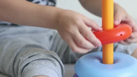The kid collects a multi-colored pyramid while sitting on the bed. Video stock 157128355