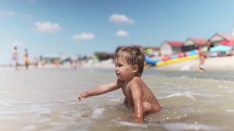 Kid collects shells and pebbles in the sea on a sandy bottom under the summer Stock Footage 348680184