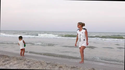 The kid collects shells and pebbles in the sea on a sandy bottom with his mother Stock Footage 348686145