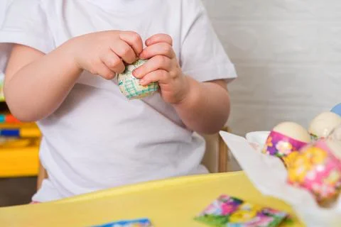 Kid decorating Easter egg with colorful shrink wrap sleeve. Child preparing Stock Photos