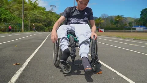 A kid with disability on his wheelchair, fitting the feet on the footrest, 스톡 동영상 185530320