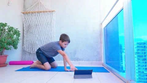 Kid doing sport exercises, doing plank exercise on yoga mat while watching video 動画素材 133458643