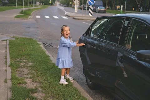 Kid with dreadlocks opens the door to a car parked along a city road on her o Stock Photos