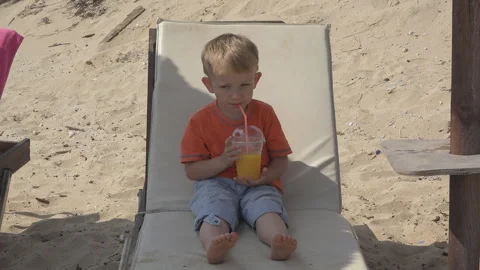 Kid drinking orange juice with straw on beach sunbed Stock Footage 255321554