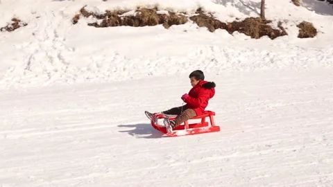 Kid drives a sledge over a snow capped slope in a winter resort Stock Footage 149857707