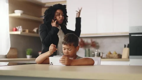 Kid eating breakfast hold smartphone while angry mother scream has work call Stock Footage 248689727