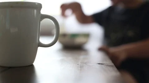 Kid eating cereal with coffee in foreground Stock Footage 79284340