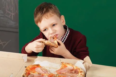 Kid eating pizza slice from the box at fast food restaurant. Stock Photos