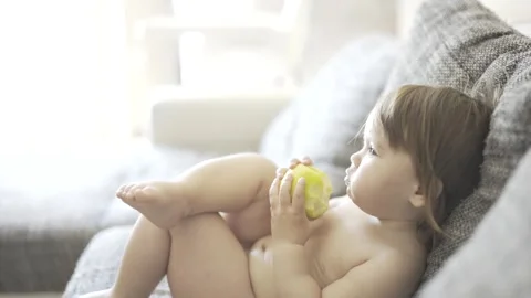 The kid eats an apple and watches TV. A little child holds a green apple in  Stock Footage 240320013
