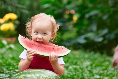 Kid eats a big piece of watermelon on the street on a summer day Stock Photos