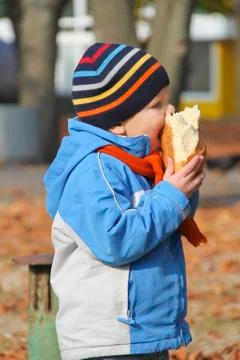 The kid eats bread during autumn walk in the park Stock Photos