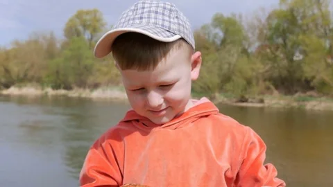 The kid eats the sausage with his teeth, strung on the willow twig with pleasure Stock Footage 75396816