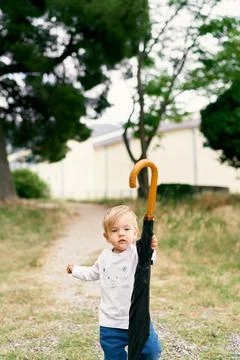 Kid with a folded umbrella stand on the path in a green park Stock Photos