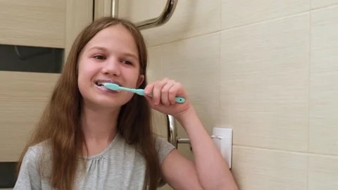 Kid girl looking at her reflection in mirror while brushing teeth in bathroom Stock Footage 264847617