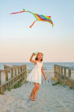 Kid girl play with rainbow colorful kite on the beach at sunset Stock Photos