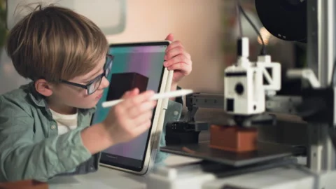 Kid in glasses operate on the tablet and observe 3D printer on the foreground Stock Footage 335380065
