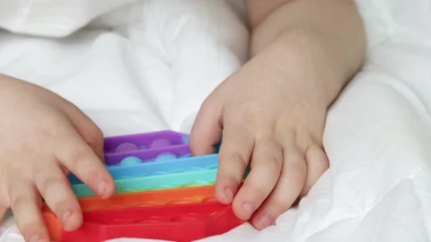 Kid hand holding playing with pop it toy in rainbow colors Видео 195211710