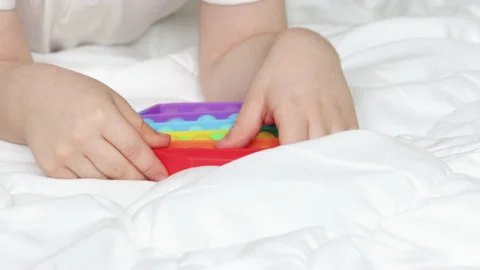 Kid hand holding playing with pop it toy in rainbow colors Stockbeeldmateriaal 195211822