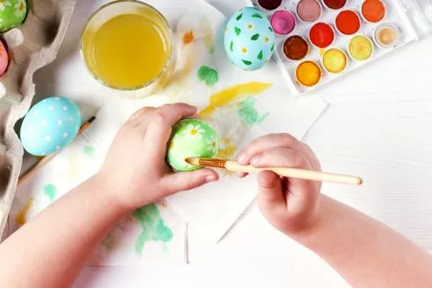 Kid hand painted Easter eggs, paints and brushes on a white table. Preparatio Stock Photos