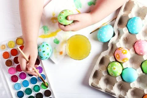 Kid hand painted Easter eggs, paints and brushes on a white table. Preparatio Stock Photos
